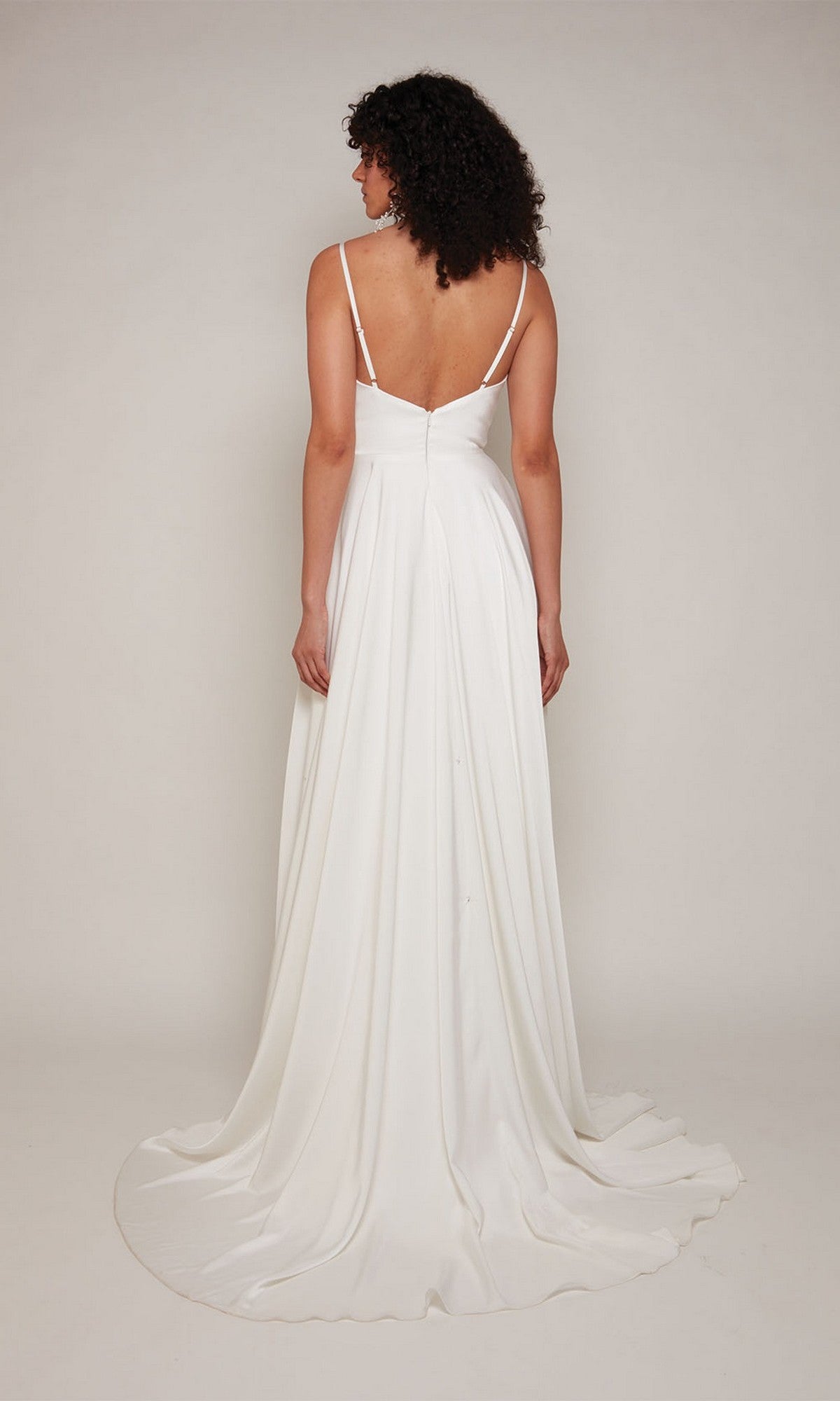 A woman faces away, wearing the Alyce 7100 long formal dress—white satin with thin straps and a flowing train—set against a plain background.